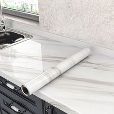 a white marble counter top next to a kitchen sink and black cabinetry with a stainless steel faucet