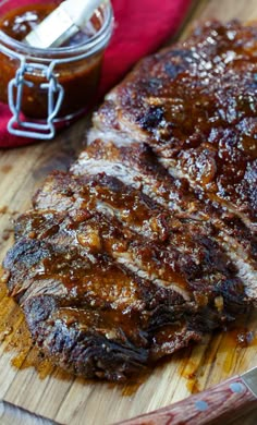 two steaks on a wooden cutting board next to a jar of bbq sauce