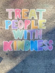 the words treat people with kindness written in multicolored letters on a concrete surface