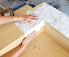 two hands on top of a piece of white tile in a room with wooden floors