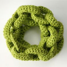 a green crocheted scarf on a white surface with the end looped up