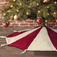 a red and white blanket on the floor under a christmas tree with ornaments around it