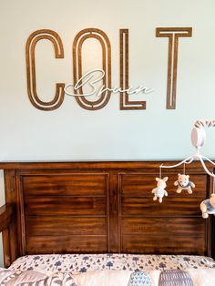 a baby crib with a teddy bear hanging from it's side and the name colt on the wall