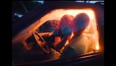 two people are sitting in a car with their hands on the steering wheel and one person is wearing gloves