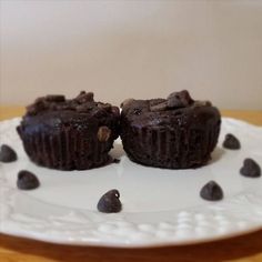 two chocolate cupcakes on a white plate with some chocolate chips around the edges