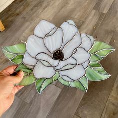 a hand holding a stained glass flower with green leaves on the bottom and white petals