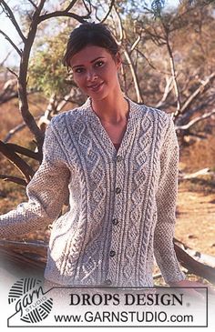 a woman wearing a cardigan and smiling for the camera in front of some trees