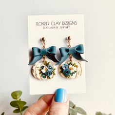 a pair of flower clay earrings with blue flowers and bows on them are being held up by a card