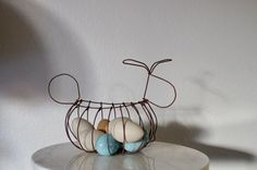 a wire sculpture with eggs in it sitting on a table next to a white wall