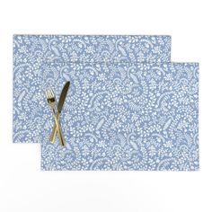 two placemats with gold forks and blue paisley print, one on top of the other