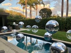 large bubbles floating in the air near a pool with grass and palm trees behind it