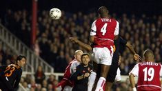 two soccer players jump to head the ball during a game in front of an audience