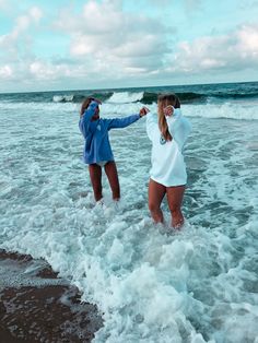 two women standing in the ocean with their arms around each other as they look into the water