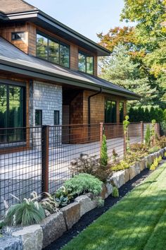 a large house with lots of windows and plants in the front yard, next to a fence