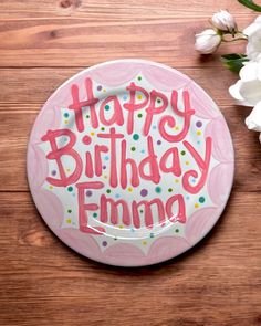 a pink plate with the words happy birthday emming on it next to some flowers