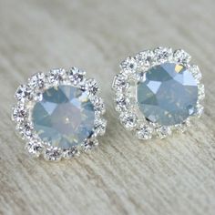 two pairs of blue and white diamond stud earrings on a wooden surface with the top one in