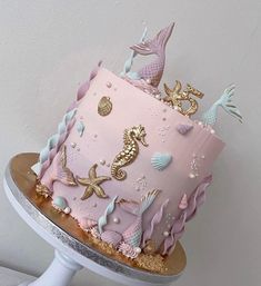 a pink and gold cake with seahorses on the top is sitting on a stand