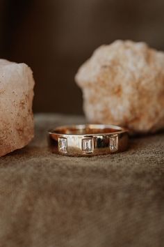 two gold wedding bands sitting on top of a rock next to a piece of crystal