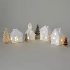 a group of small white houses with christmas trees in the foreground and lights on them