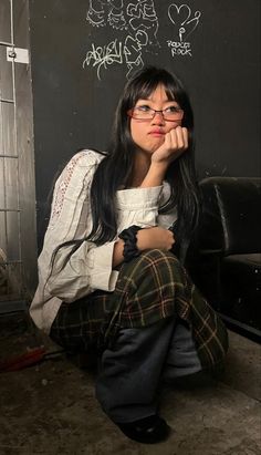 a woman sitting on the ground in front of a black wall with graffiti written on it