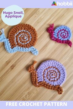 three crocheted snail appliques sitting on top of a wooden floor next to each other