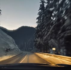 a car driving down a snow covered road next to tall trees and mountains in the distance