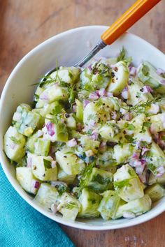 a white bowl filled with cucumber and red onion salad on top of a wooden table