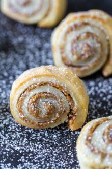 several cinnamon rolls on a black surface covered in powdered sugar and sprinkles