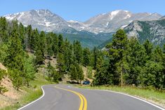 an empty road in the mountains with trees on both sides and a car driving down it