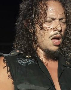 a close up of a person with long hair wearing a black shirt and holding a microphone