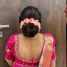 a woman wearing a pink sari with flowers in her hair is standing near a door