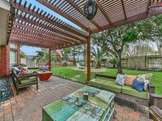 a covered patio with couches and tables in the back yard, surrounded by trees