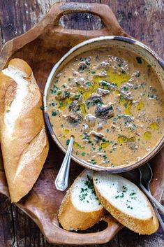 a wooden bowl filled with soup next to bread on top of a cutting board and spoons