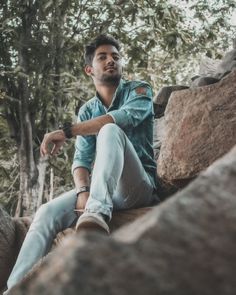 a man sitting on top of a rock next to trees