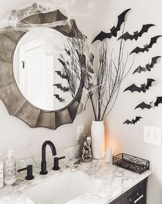 a bathroom decorated for halloween with bats hanging on the wall and a mirror above it