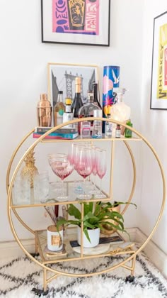 a gold bar cart filled with glasses and bottles on top of a rug next to pictures