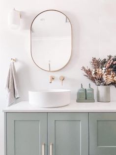 a white sink sitting under a round mirror next to a green cabinet and counter top