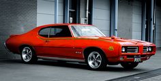 an orange muscle car parked in front of a building