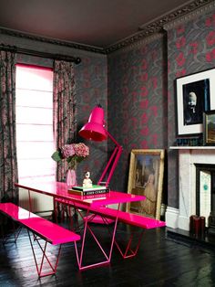 a pink table and bench in a room with dark walls, wood flooring and paintings on the wall