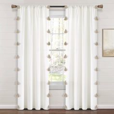 a white curtain with tassels hanging on the side of it in front of a window