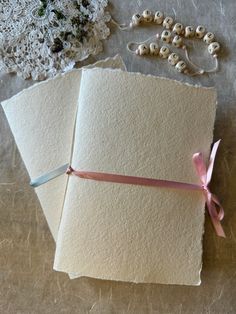 two pieces of paper with pink ribbon tied to them on a table next to beads