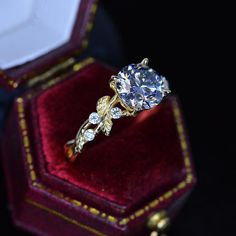 an engagement ring in a red velvet box with gold trimmings and diamond accents