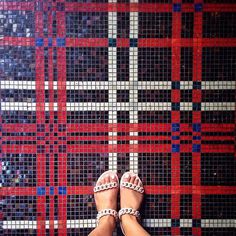 a woman's feet with sandals on standing in front of a tiled wall and floor