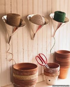 several pots are lined up on the wall with scissors and yarn in them, along with two crochet hooks