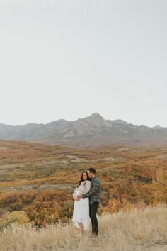 a man and woman standing on top of a grass covered field with mountains in the background