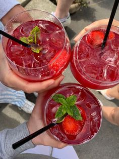 three people holding up glasses with strawberries in them