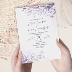 a person holding up a wedding card in front of a wicker basket with flowers on it