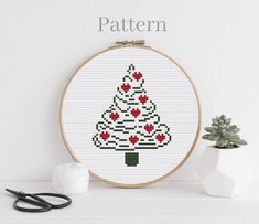 a cross stitch christmas tree with poinsettis is shown in front of a potted plant