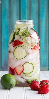 a person pouring water into a jar filled with cucumbers and strawberries