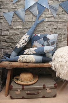 a pile of pillows sitting on top of a wooden bench next to a hat and suitcase